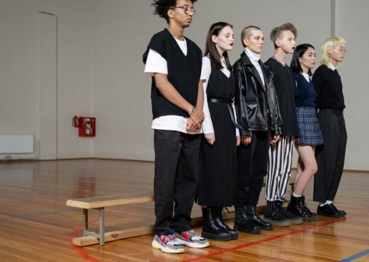 Diverse group of stylish teenagers standing in a gym, showcasing modern fashion trends.