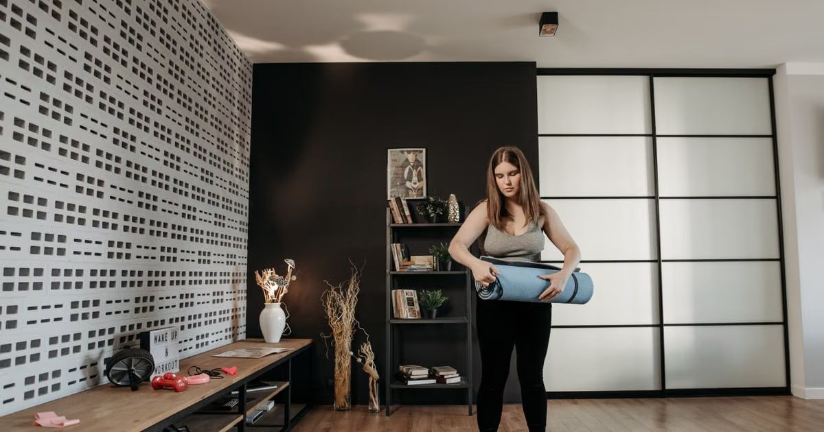 Plus size woman rolling a yoga mat in a stylish indoor setting with modern decor.