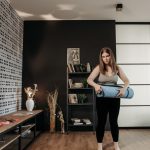 Plus size woman rolling a yoga mat in a stylish indoor setting with modern decor.