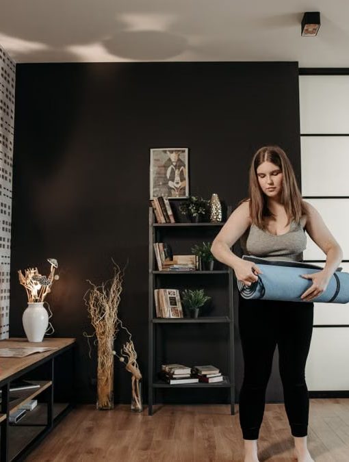 Plus size woman rolling a yoga mat in a stylish indoor setting with modern decor.