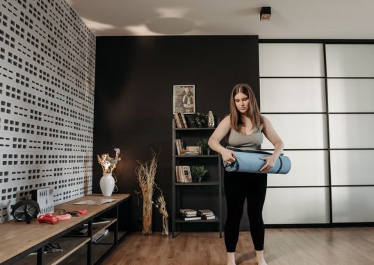 Plus size woman rolling a yoga mat in a stylish indoor setting with modern decor.