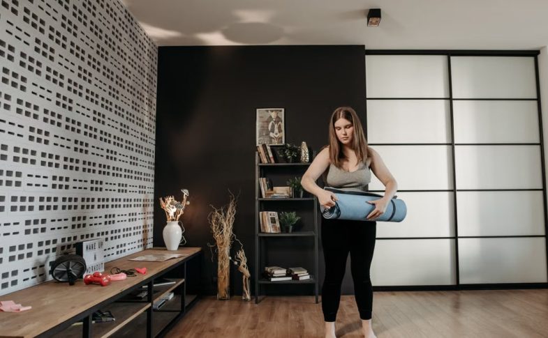 Plus size woman rolling a yoga mat in a stylish indoor setting with modern decor.